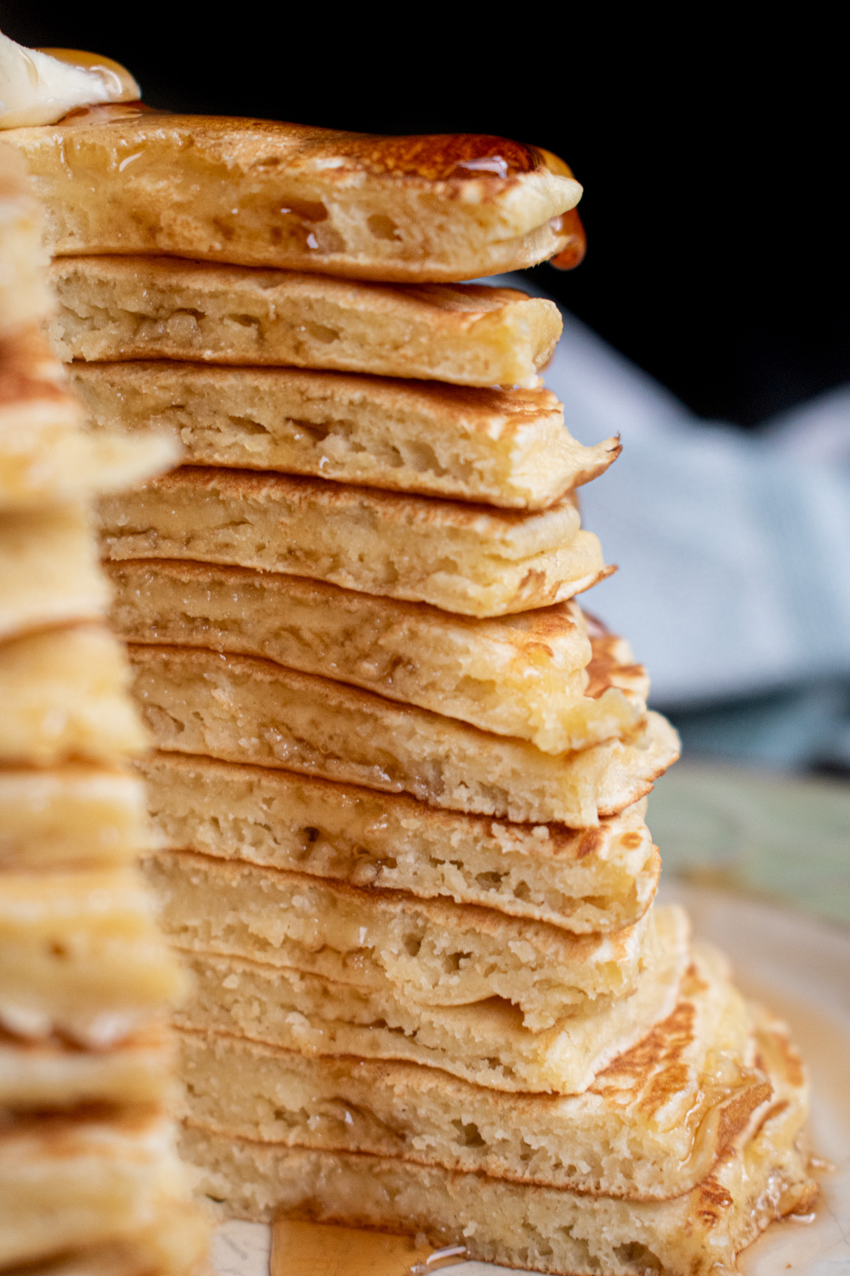 Oat milk pancakes stacked high with a slice cut out to show the fluffy texture with butter and maple syrup dripping down the sides.
