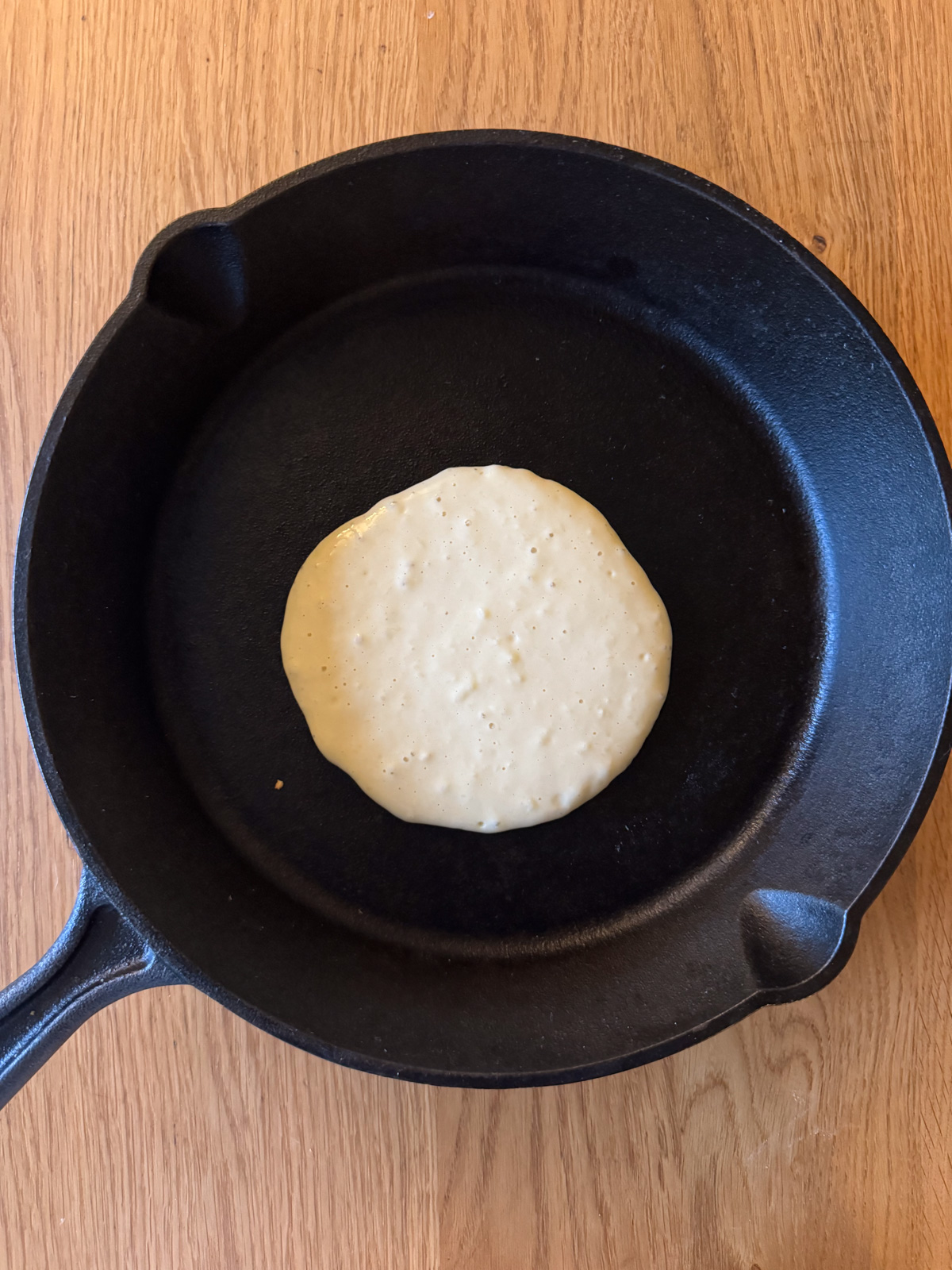 Oat milk pancake in a cast iron pan being cooked with batter side up. 