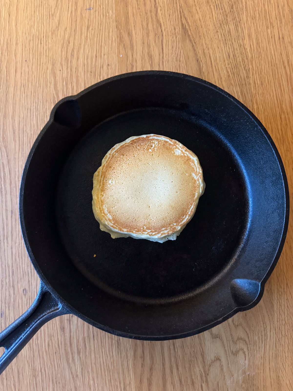 Oat milk pancake in a cast iron pan being cooked with done side up.