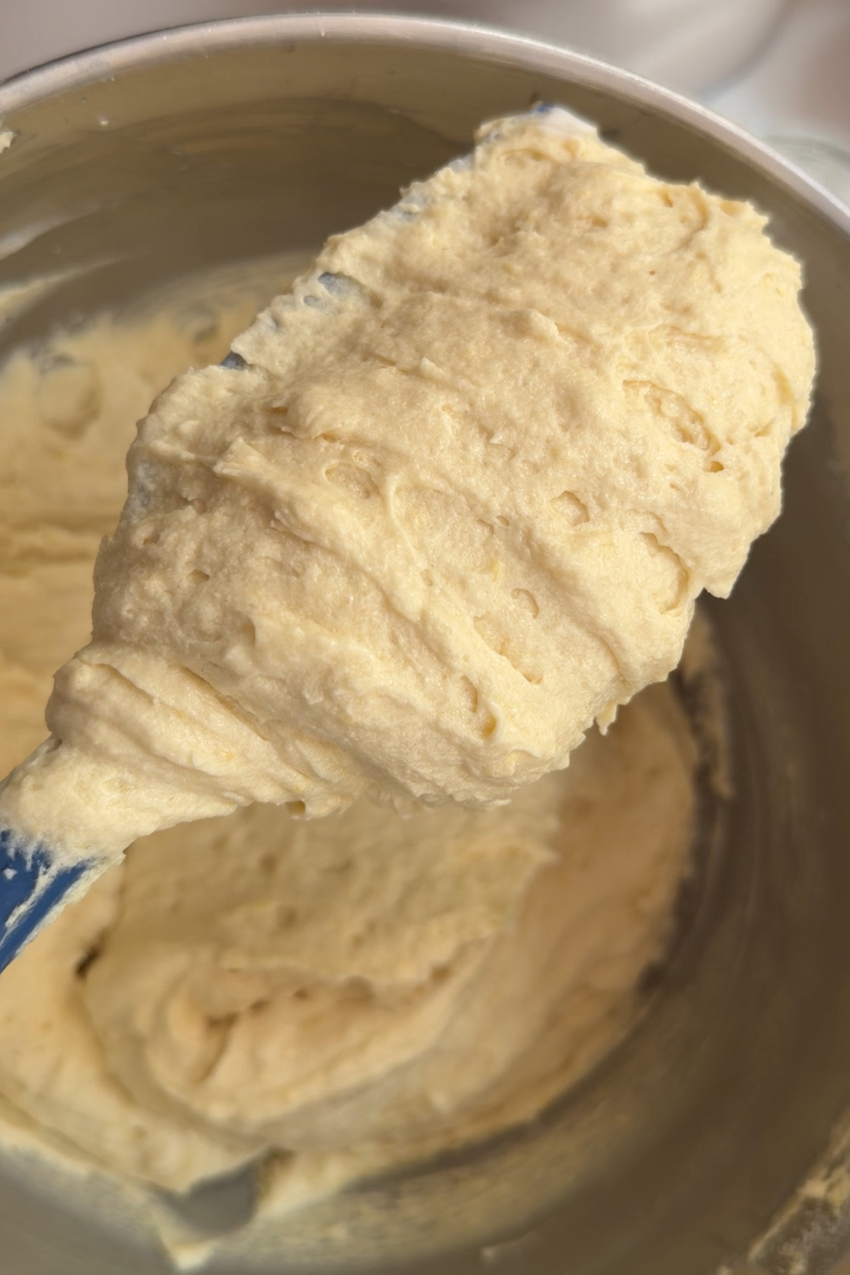 Picture of the cake batter for for lemon blueberry mascarpone cake on a rubber spatula to show texture.
