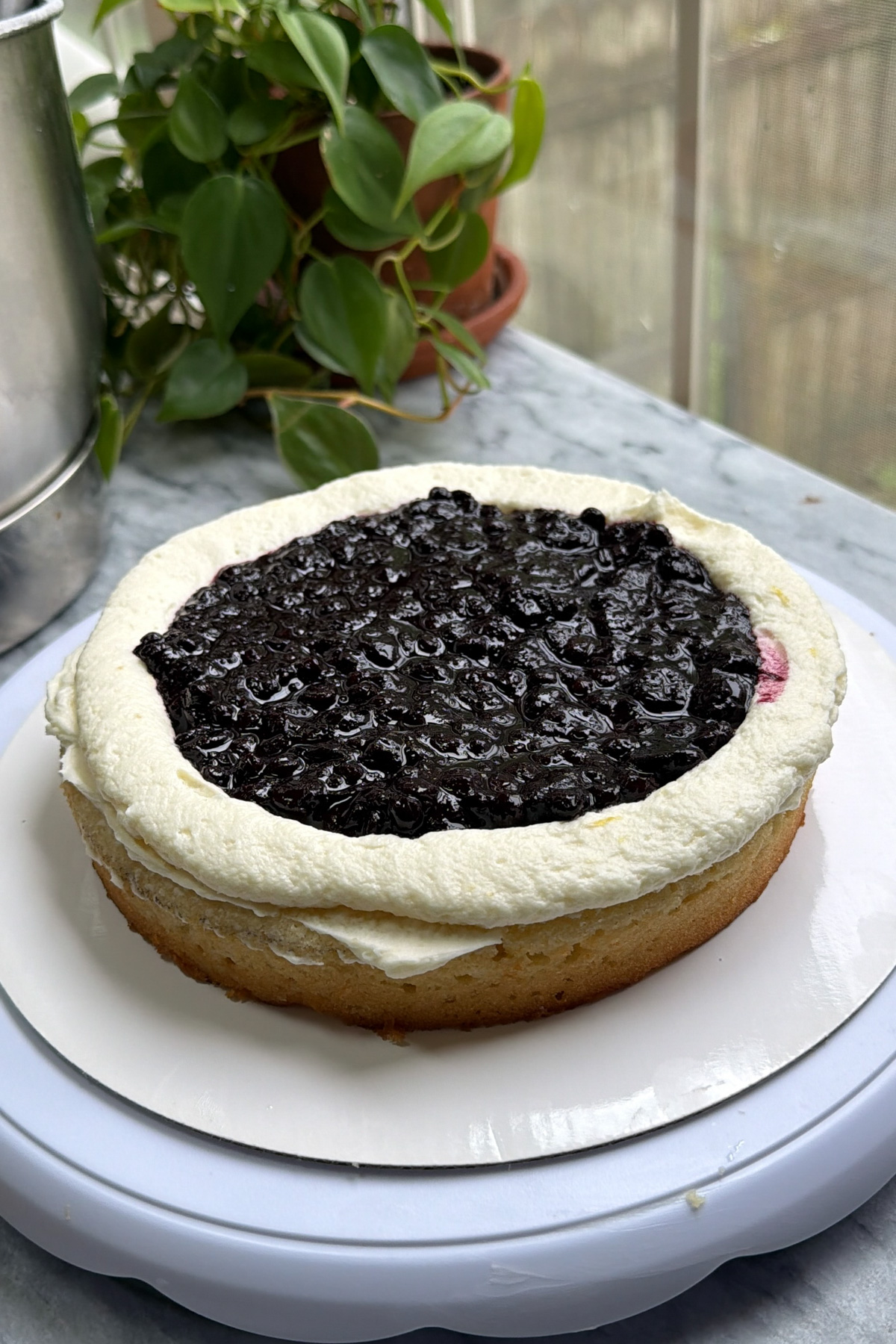 Lemon blueberry mascarpone cake being assembled, showing a frosting dam with the blueberry compote in the middle.