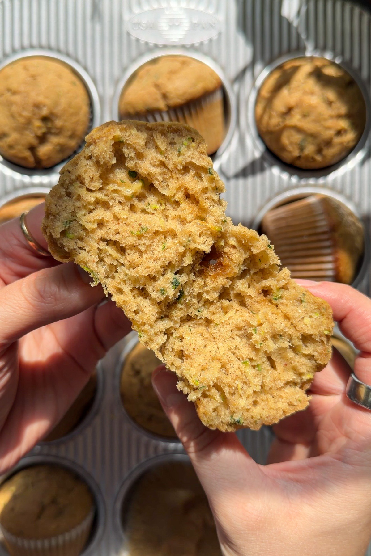 Hand holding a sourdough zucchini muffin that has been ripped in half, showing the inside of the muffins.