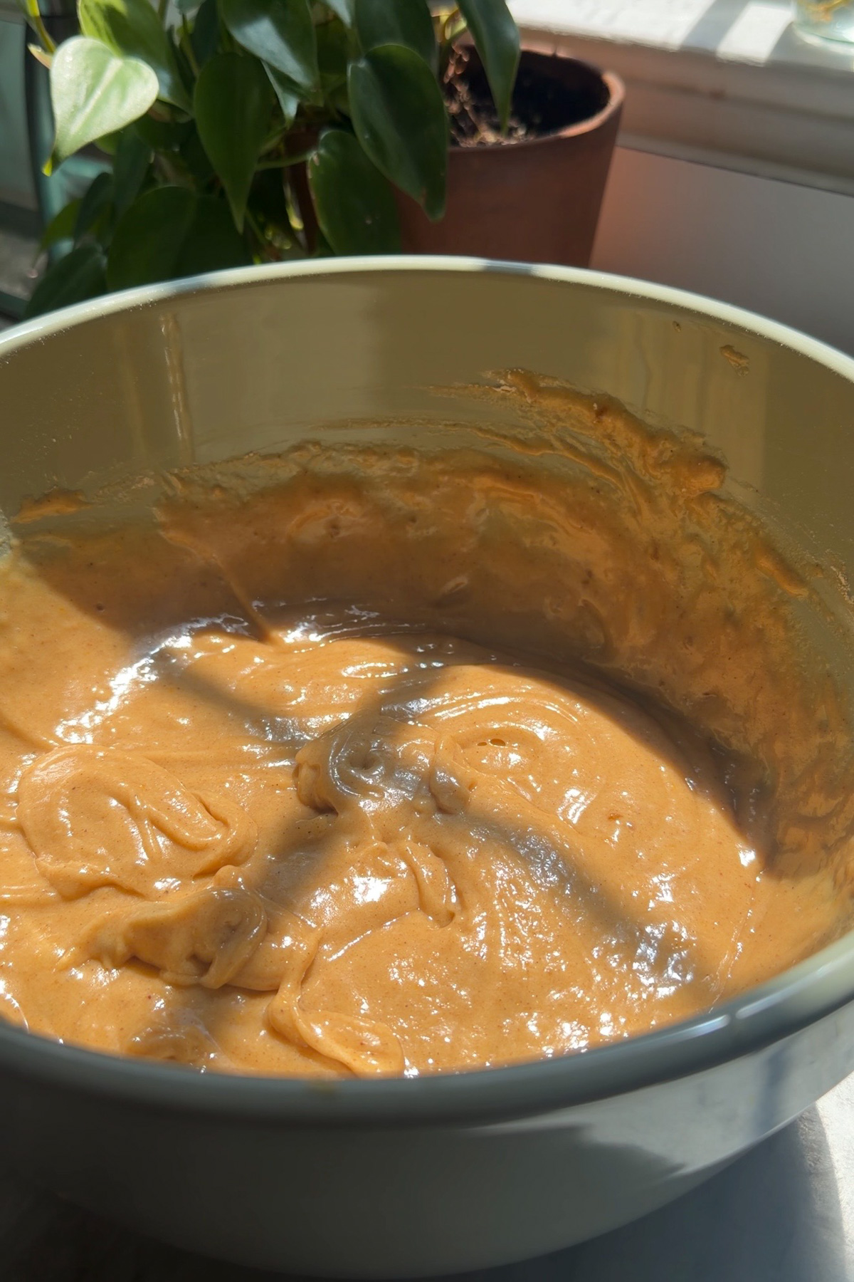 The batter for sourdough discard zucchini muffins in a ceramic mixing bowl with a plant in the background.