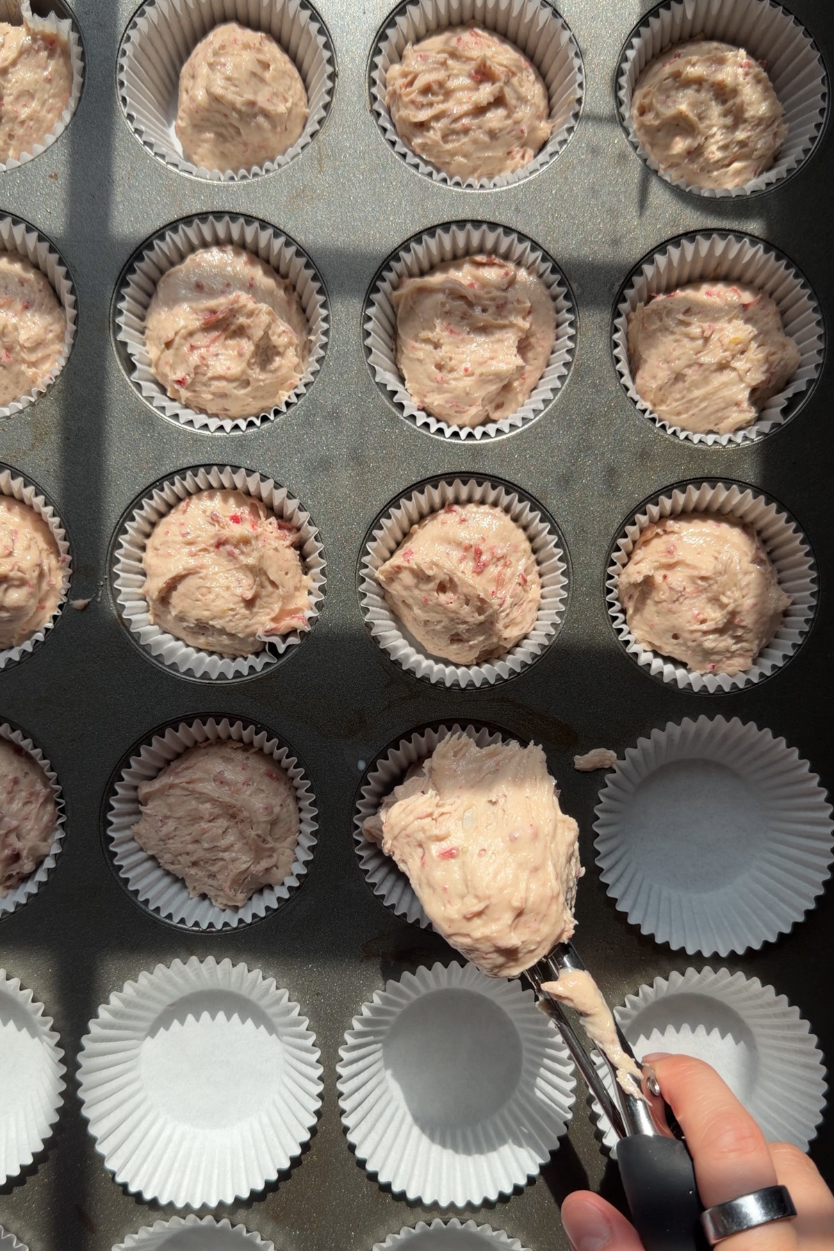 Strawberry crunch cupcake batter being portioned into cupcake liners before baking.