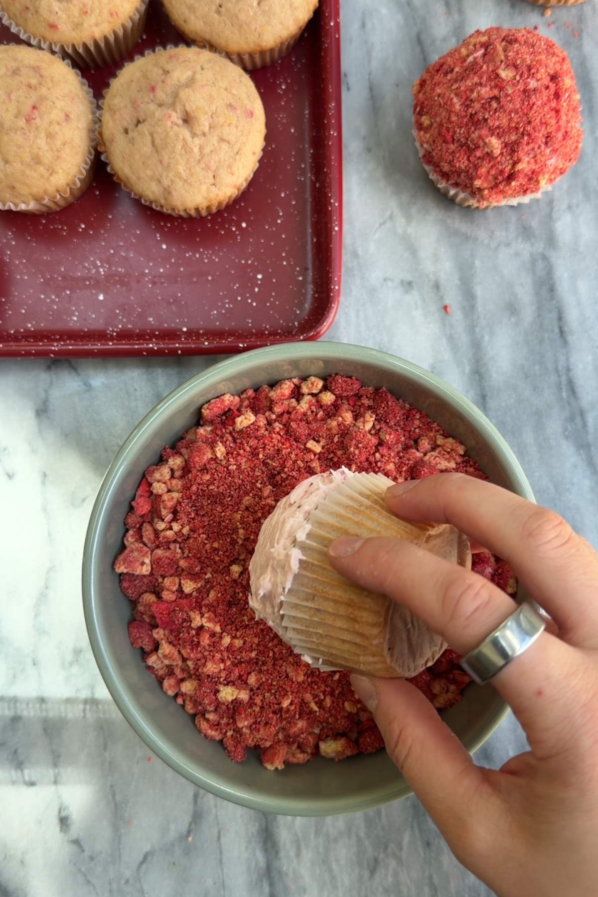 Hand holding a strawberry crunch cupcake with more cupcakes in the background.