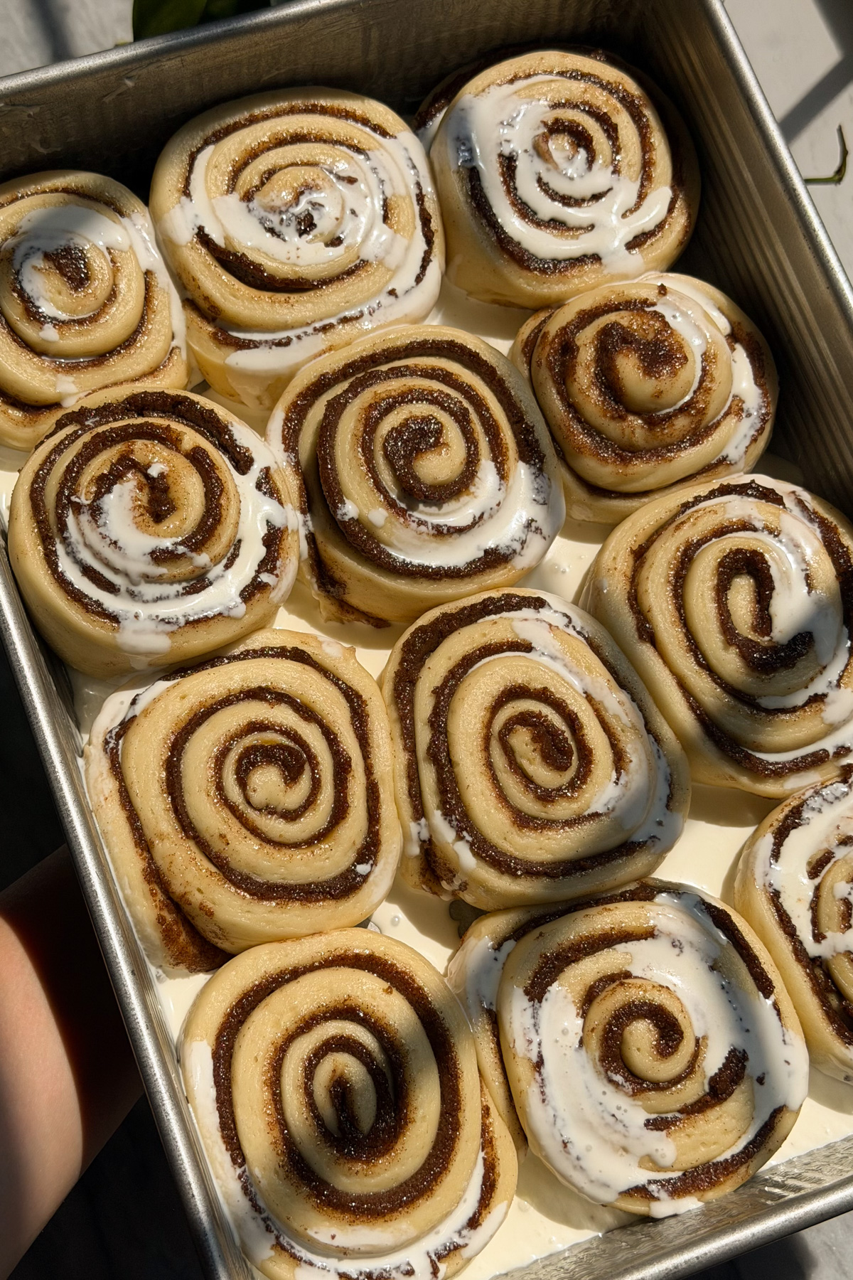 Sourdough discard cinnamon rolls before baking with heavy cream poured on the rolls.