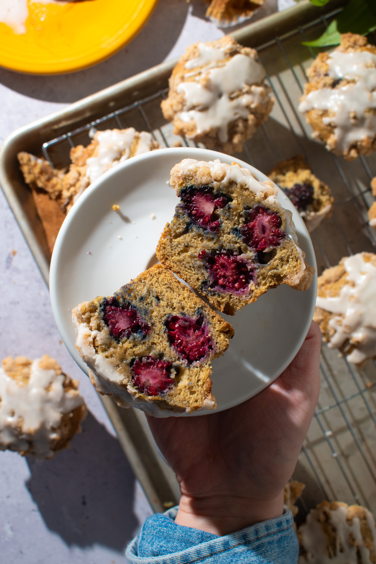 Picture of a hand holding a banana blackberry muffin with muffins in the background. 
