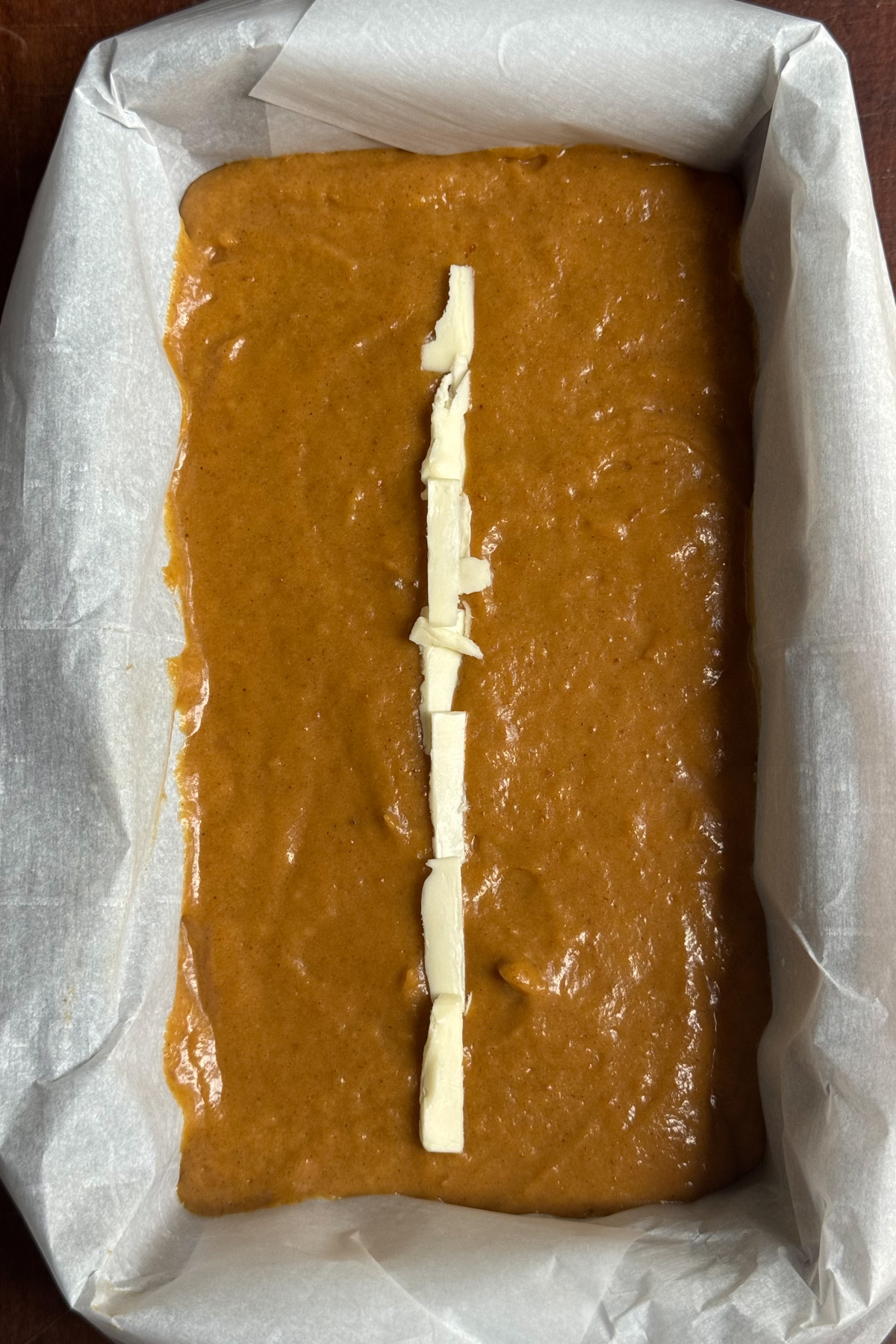 Picture of sourdough pumpkin bread batter in a lined loaf pan with a strip of butter down the middle.
