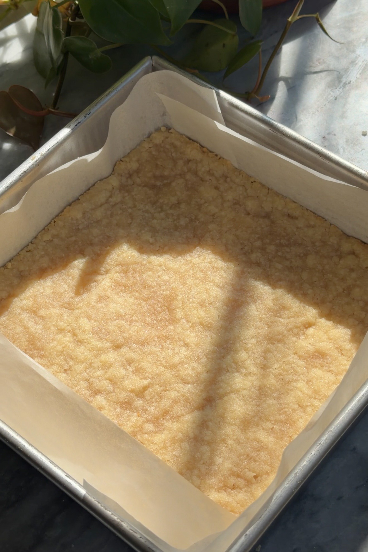 Pre-baked shortbread crust in a lined 8x8 pan for apple pie crumb bars.
