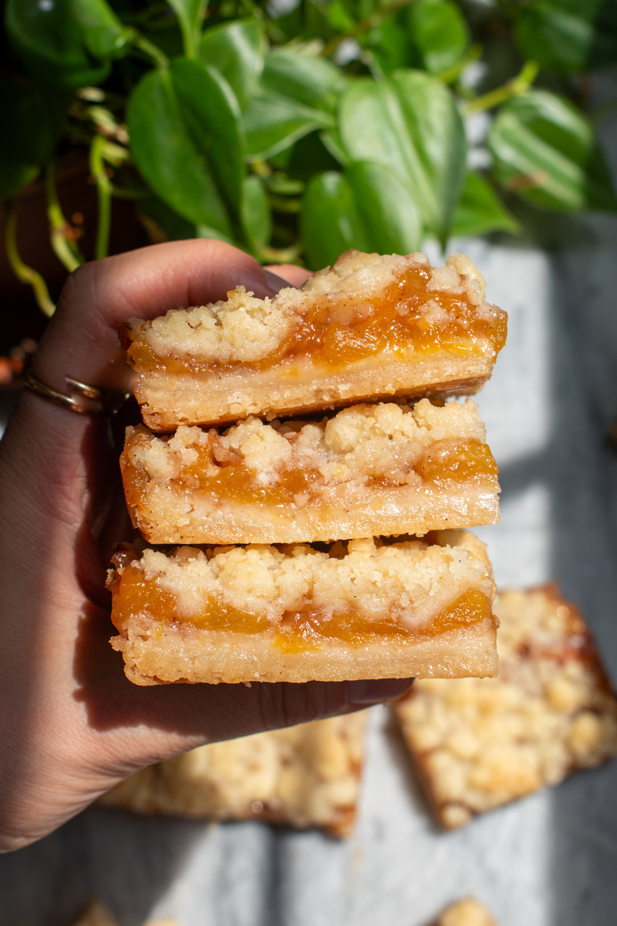 A hand holding three peach crumb bars stacked on top of each other to show the layers.