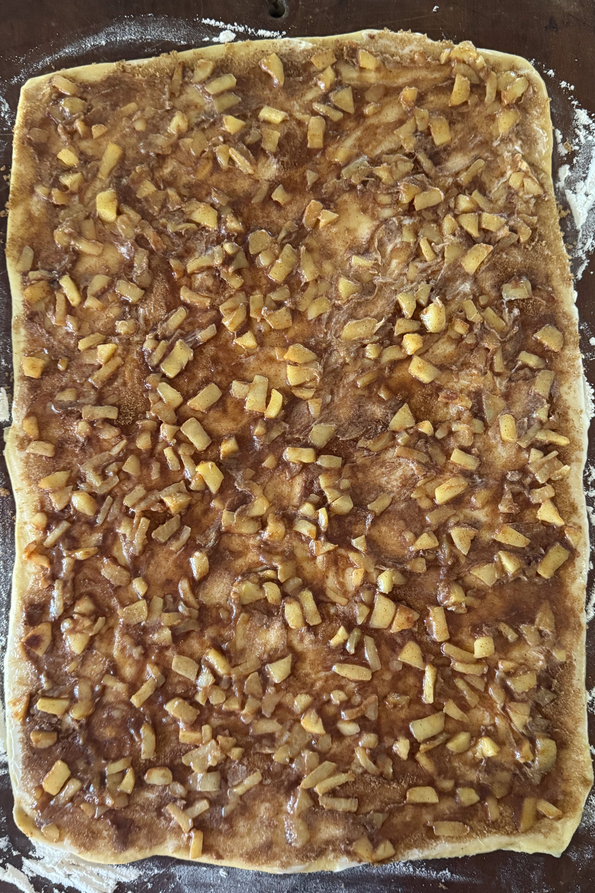 Picture of cinnamon roll dough rolled out and covered with cinnamon sugar and apple pie filling for apple pie cinnamon rolls.