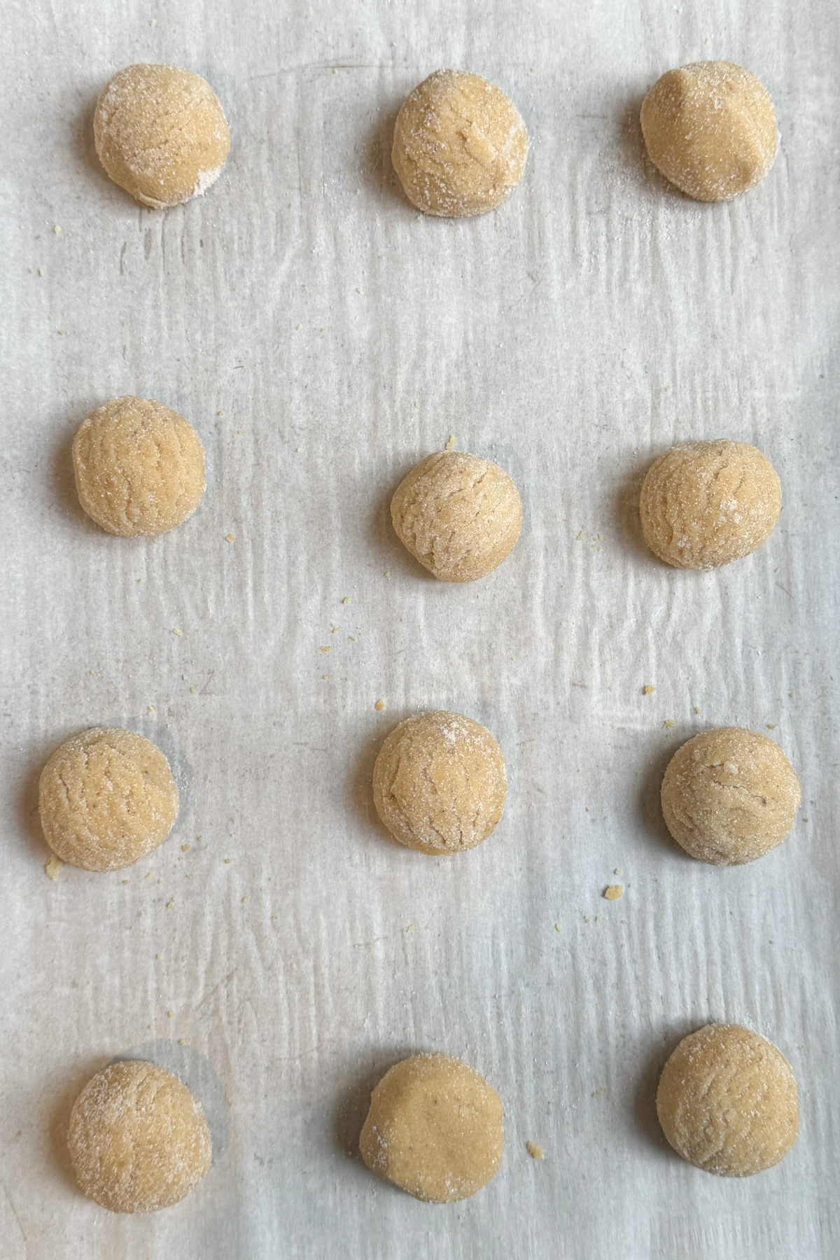 Picture of brown butter sugar cookie dough balls, rolled in sugar on a parchment paper-lined baking sheet. 