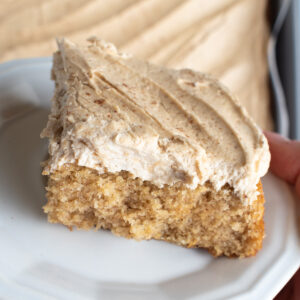 Picture of a hand holding a piece of vanilla chai sheet cake with espresso buttercream on a white plate.