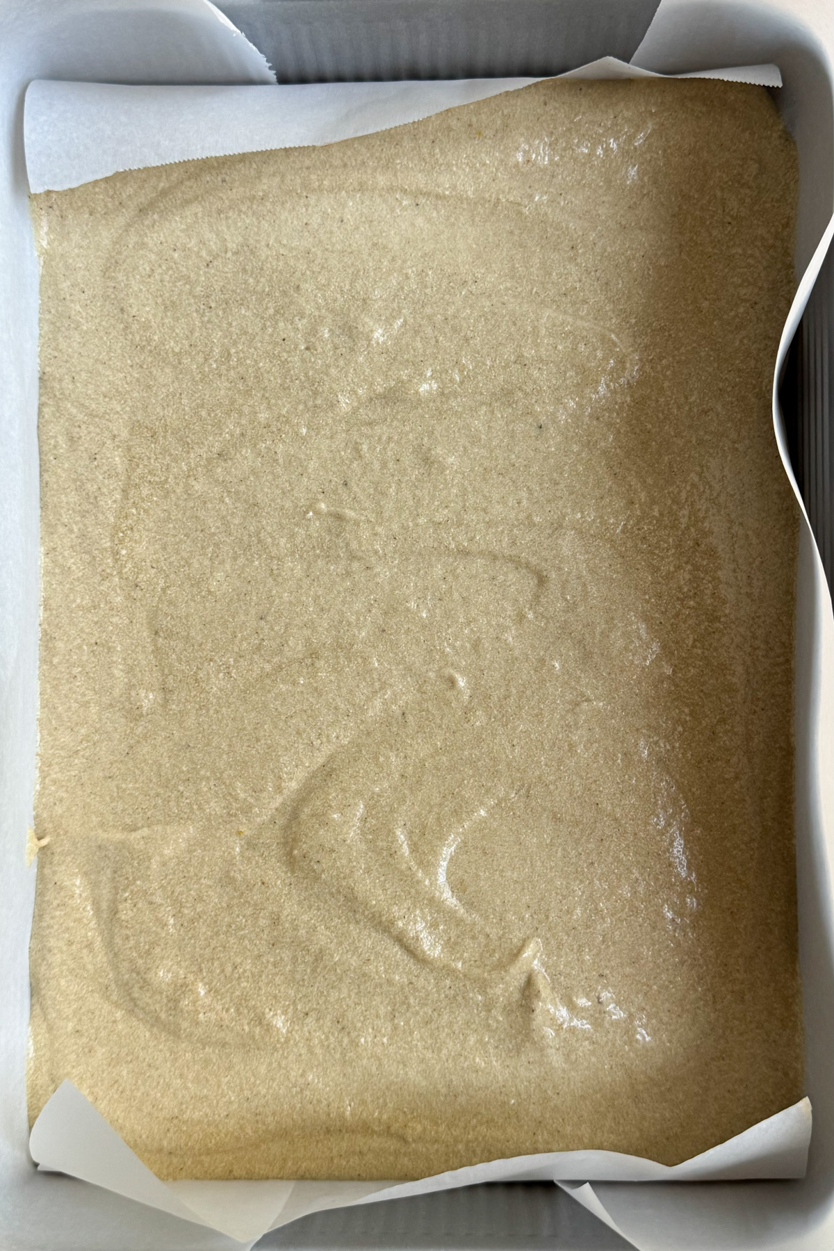 Picture of chai cake batter in a lined 9x13 pan before being baked into vanilla chai cake with espresso buttercream.