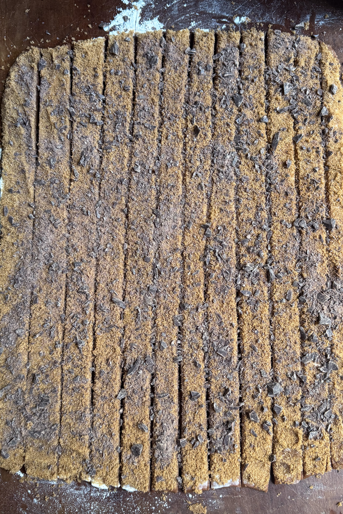 Overhead picture of chocolate cinnamon roll dough rolled out and covered in cinnamon sugar and chopped chocolate before being cut into strips for chocolate cinnamon rolls with cinnamon espresso cream cheese frosting.