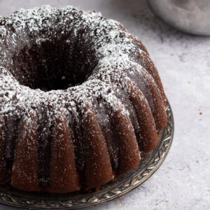 Picture of chocolate sour cream pound cake topped with chocolate ganache and powdered sugar.