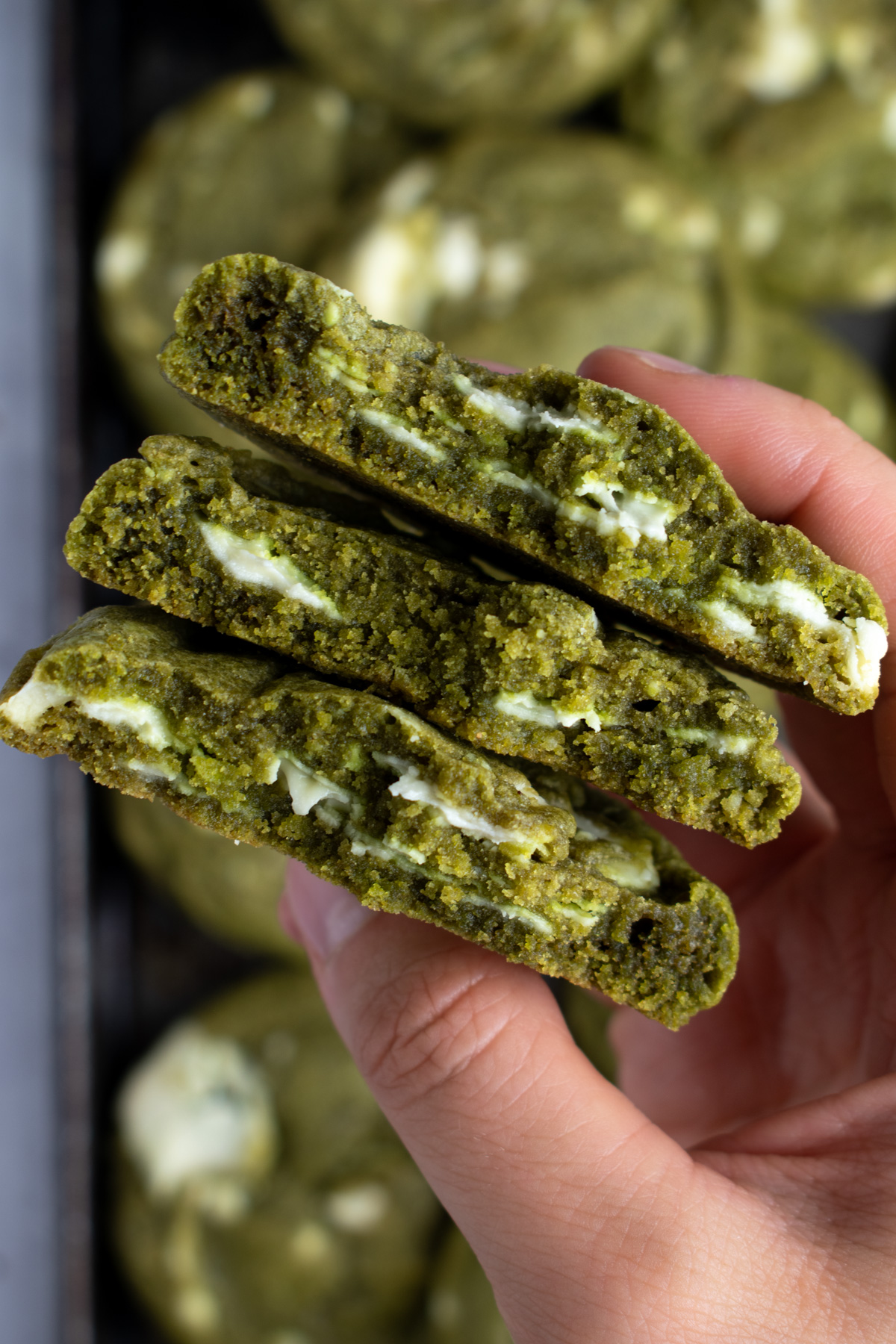 Overhead picture of a hand holding 3 matcha white chocolate cookie halves stacked on top of each other.