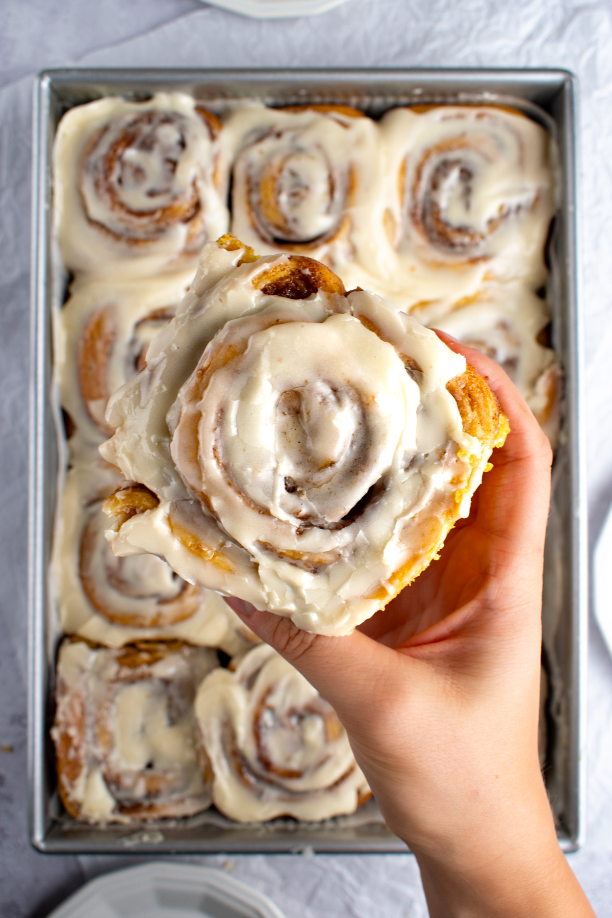 A hand holding pumpkin cream cheese cinnamon rolls with more cinnamon rolls in the background.
