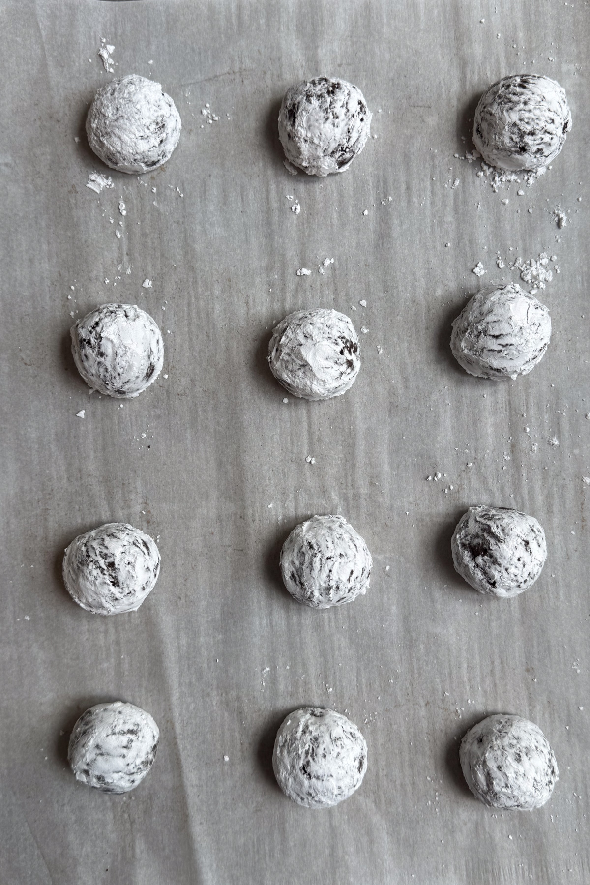 Overhead picture of chilled sourdough chocolate crinkle cookie dough balls, rolled in powdered sugar, and placed on a parchment-lined baking sheet.
