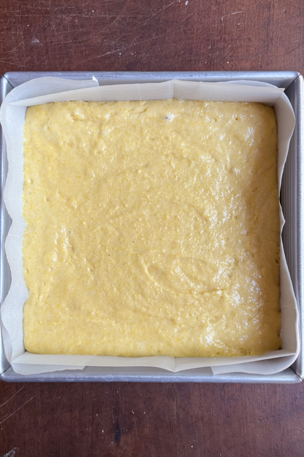 Overhead picture of sourdough discard cornbread batter in a lined 8x8 baking pan.