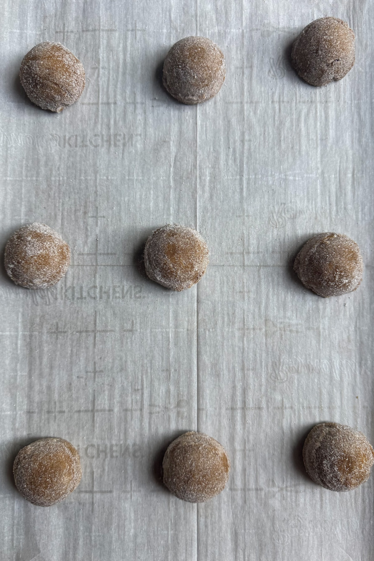 Overhead picture of sourdough gingerbread cookie dough balls, rolled in sugar, and placed on a parchment-lined baking sheet.