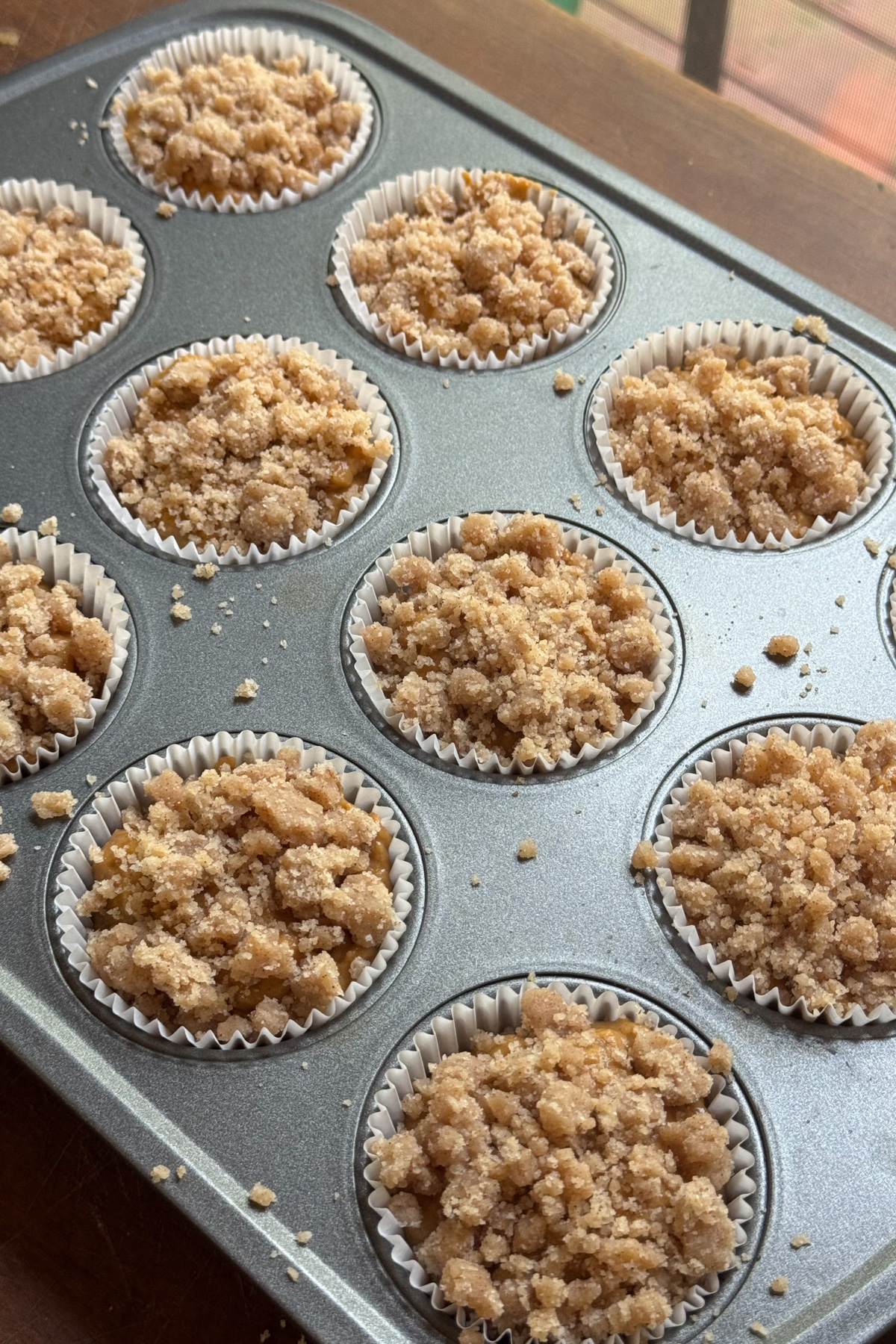 Picture of sourdough pumpkin banana muffin batter topped with cinnamon streusel in a lined 12-muffin pan before baking.