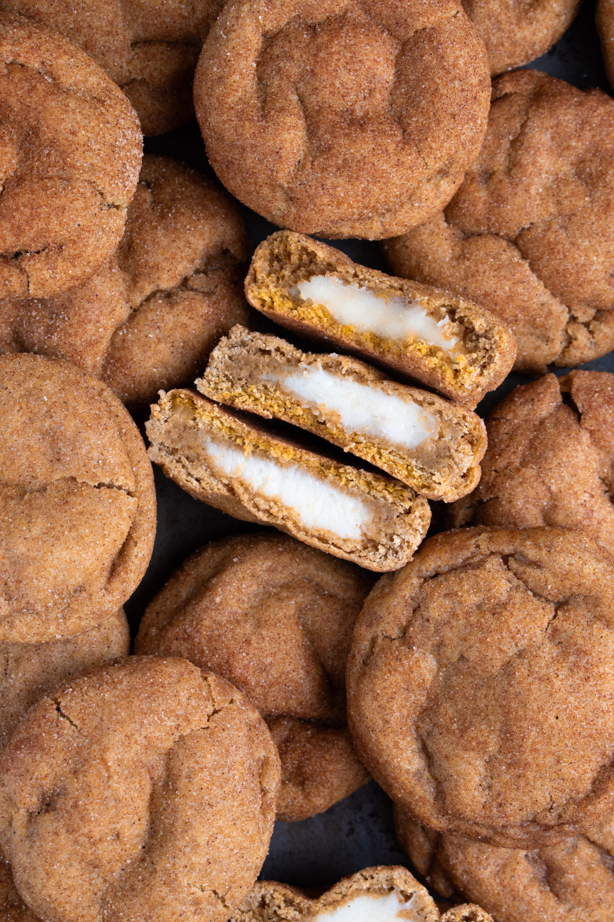 Picture of sourdough pumpkin cheesecake cookies on a baking tray with 3 halves stacked on their sides to show the cheesecake filling.