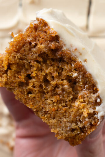 Overhead picture of a hand holding a slice of sourdough discard carrot snack cake.