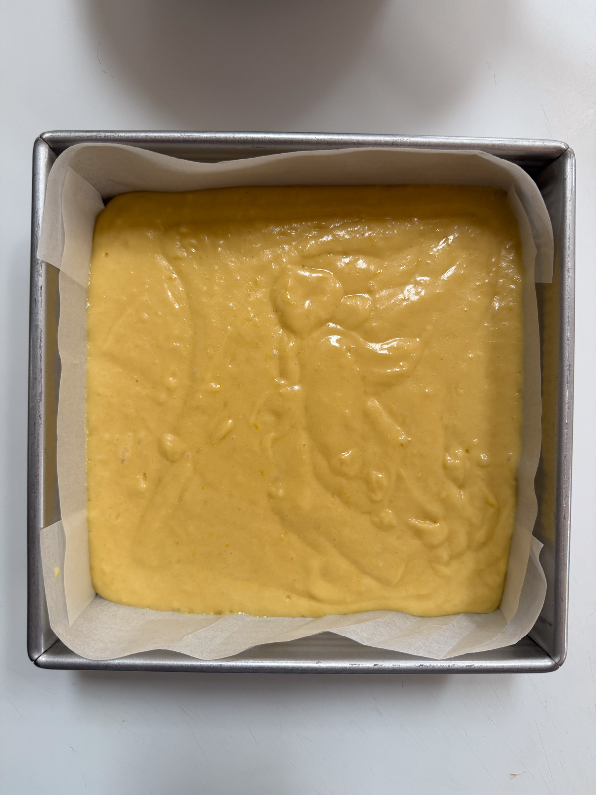 Overhead picture of sourdough discard lemon snack cake batter in a lined 8x8 pan before baking. 