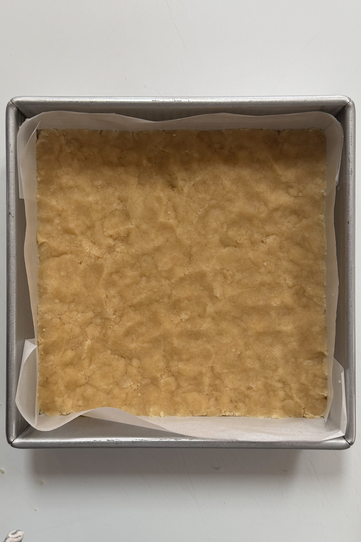 Picture of blueberry crumb bar dough pressed into a lined 8x8 pan.