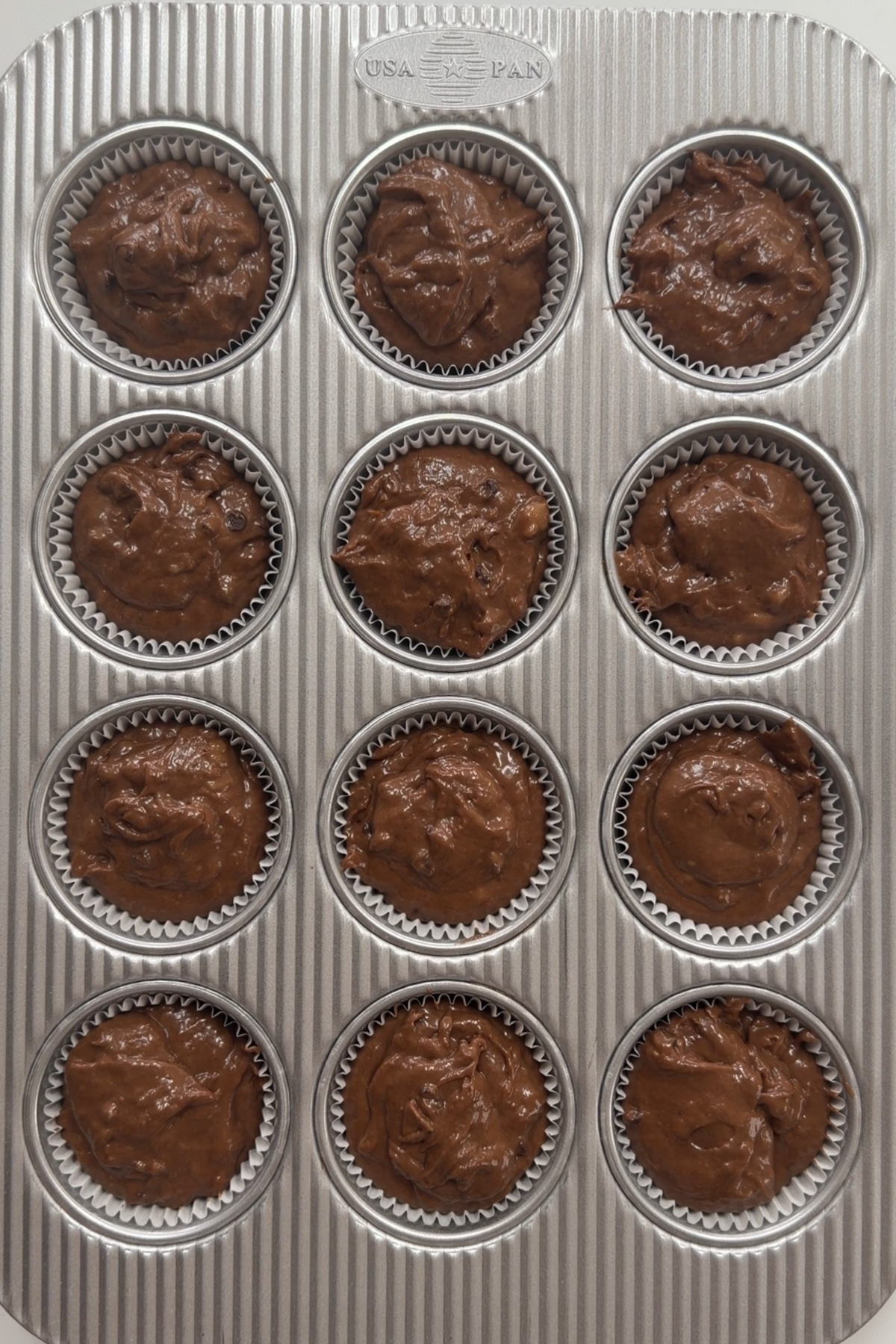 Overhead picture of sourdough chocolate banana muffin batter in a 12-muffin pan before baking.