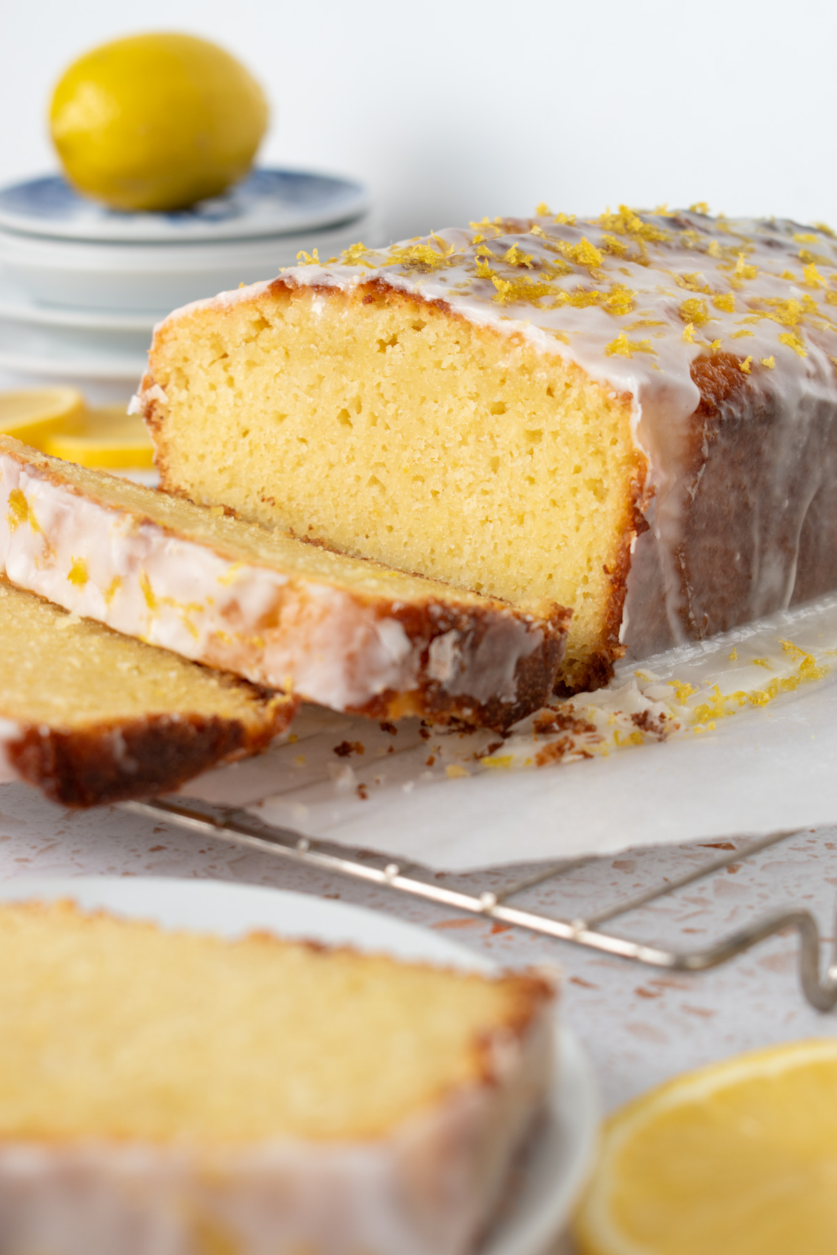 Picture of a glazed sourdough lemon pound cake on a parchment lined cooling rack with a lemon behind it.