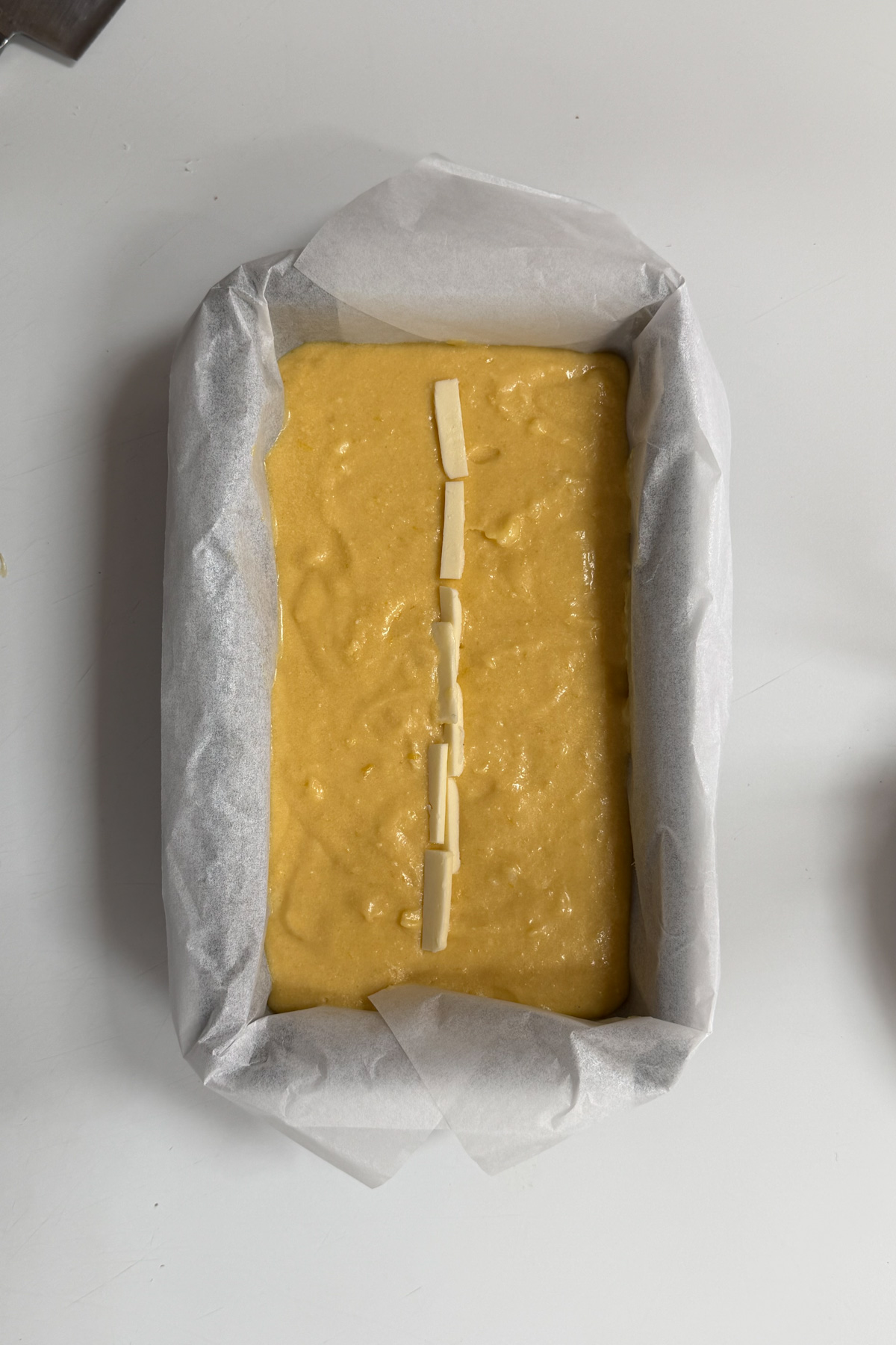 Picture of sourdough lemon pound cake in a loaf pan before baking. It has a line of cold butter going straight down the middle.