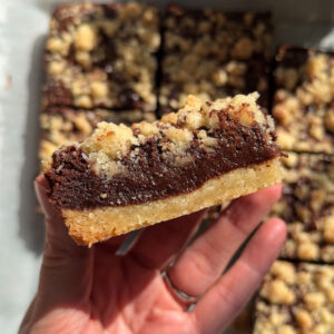 Overhead image of a hand holding a brownie crumb bar showing its layers with more crumb bars laying flat in the background.