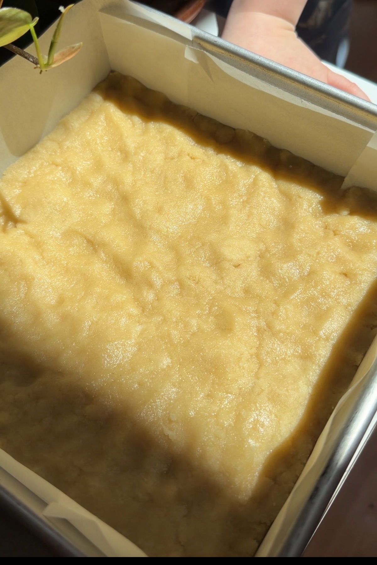 Picture of an unbaked shortbread crust pressed into the bottom of an 8x8 pan for brownie crumb bars.