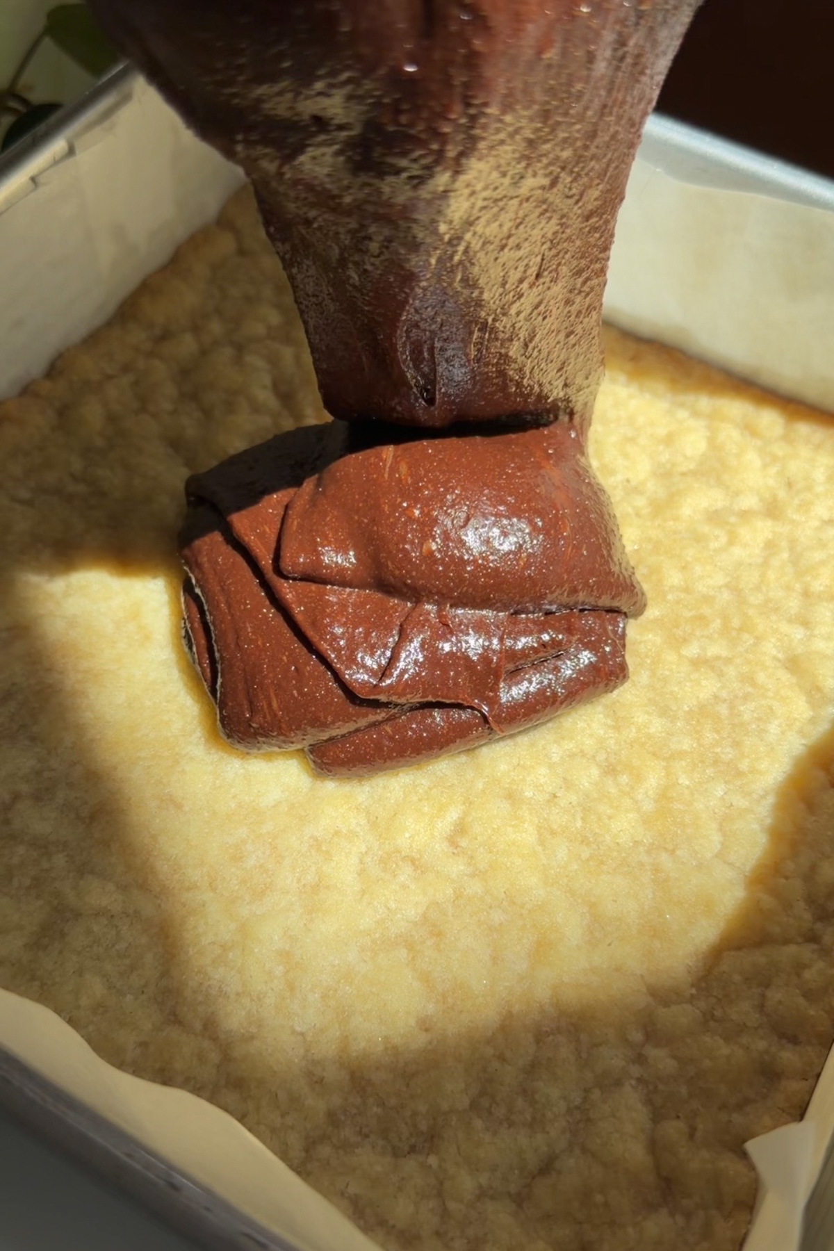 Picture of brownie batter being poured onto a par-baked shortbread crust for brownie crumb bars.