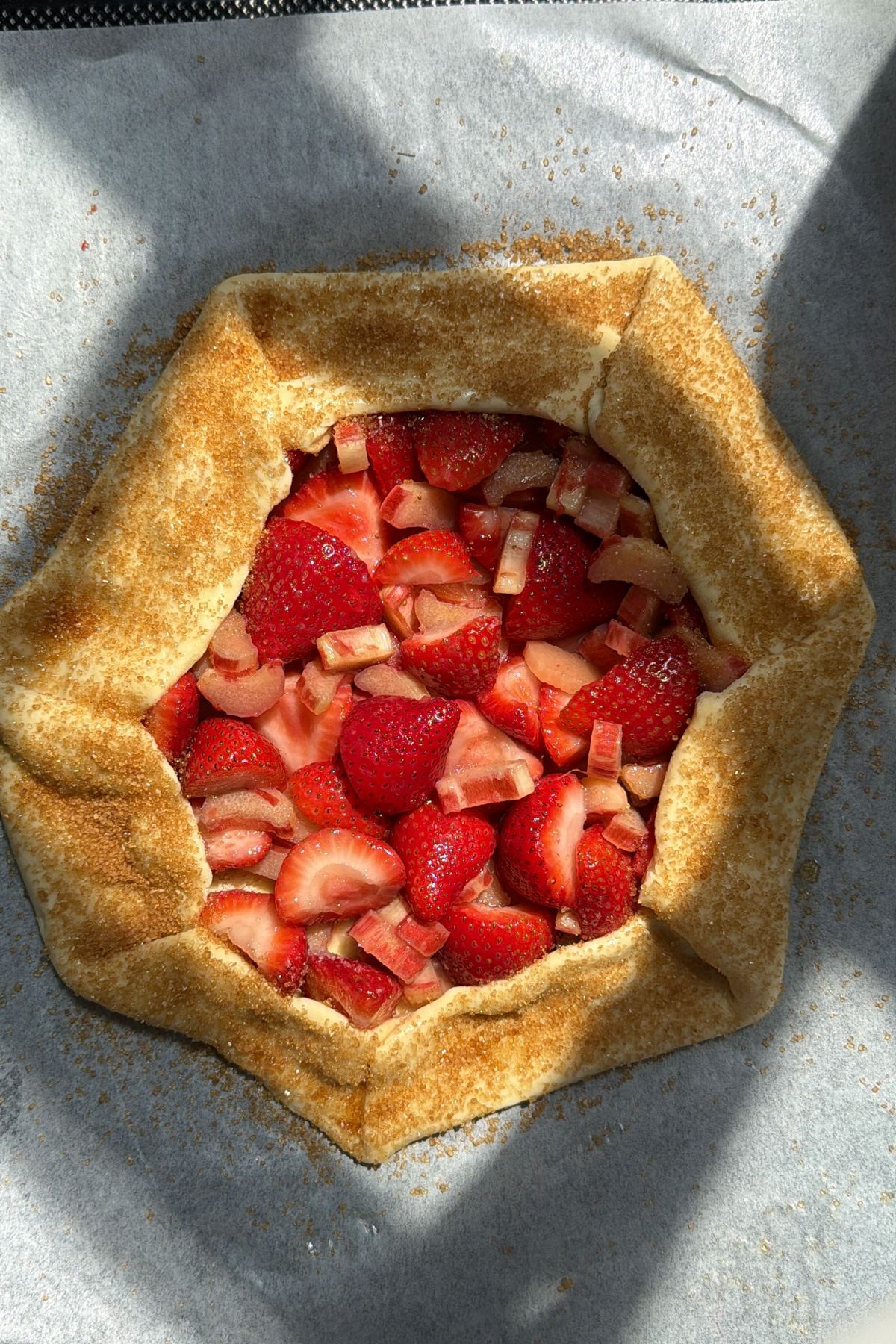 Overhead picture of a strawberry rhubarb galette topped with turbinado sugar before baking.