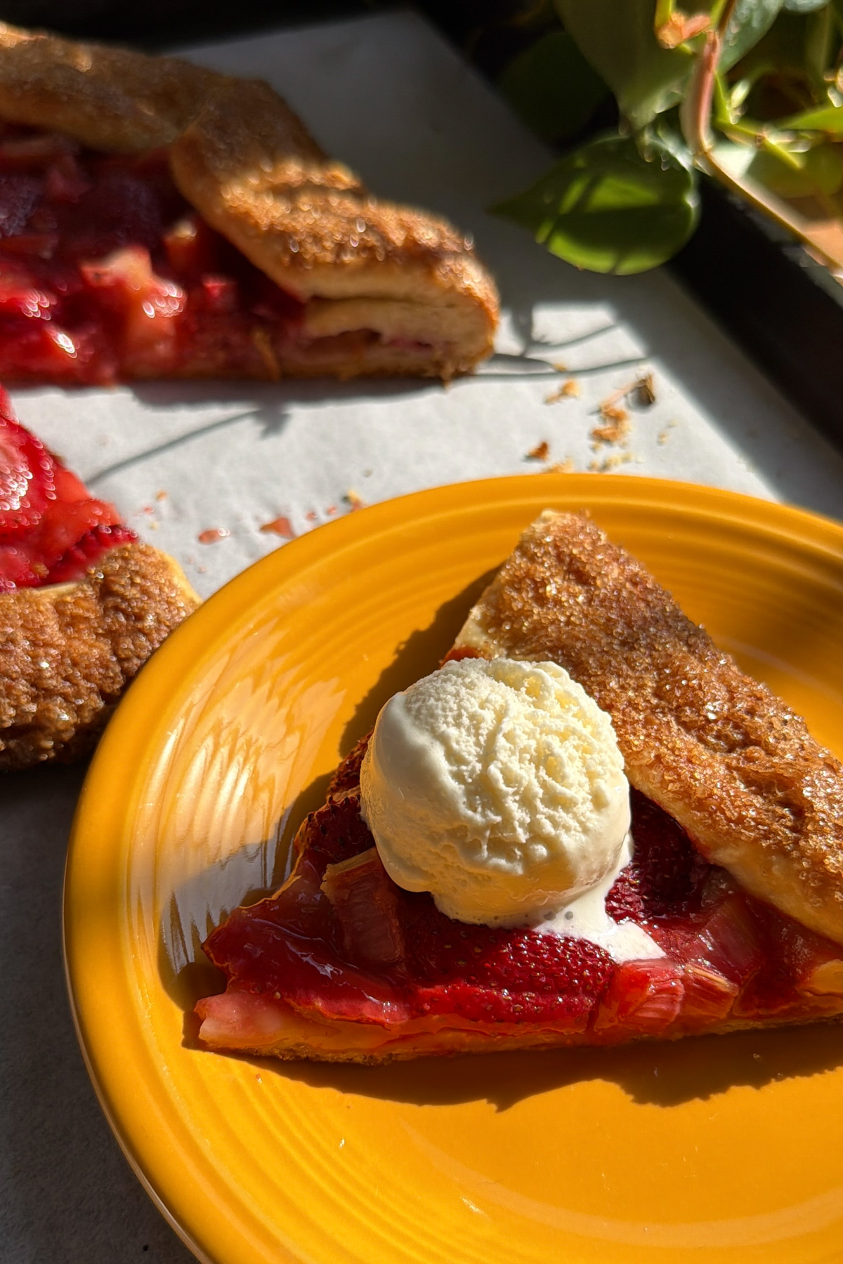 Picture of a strawberry rhubarb galette slice with a scoop of melting whipped cream on top. 