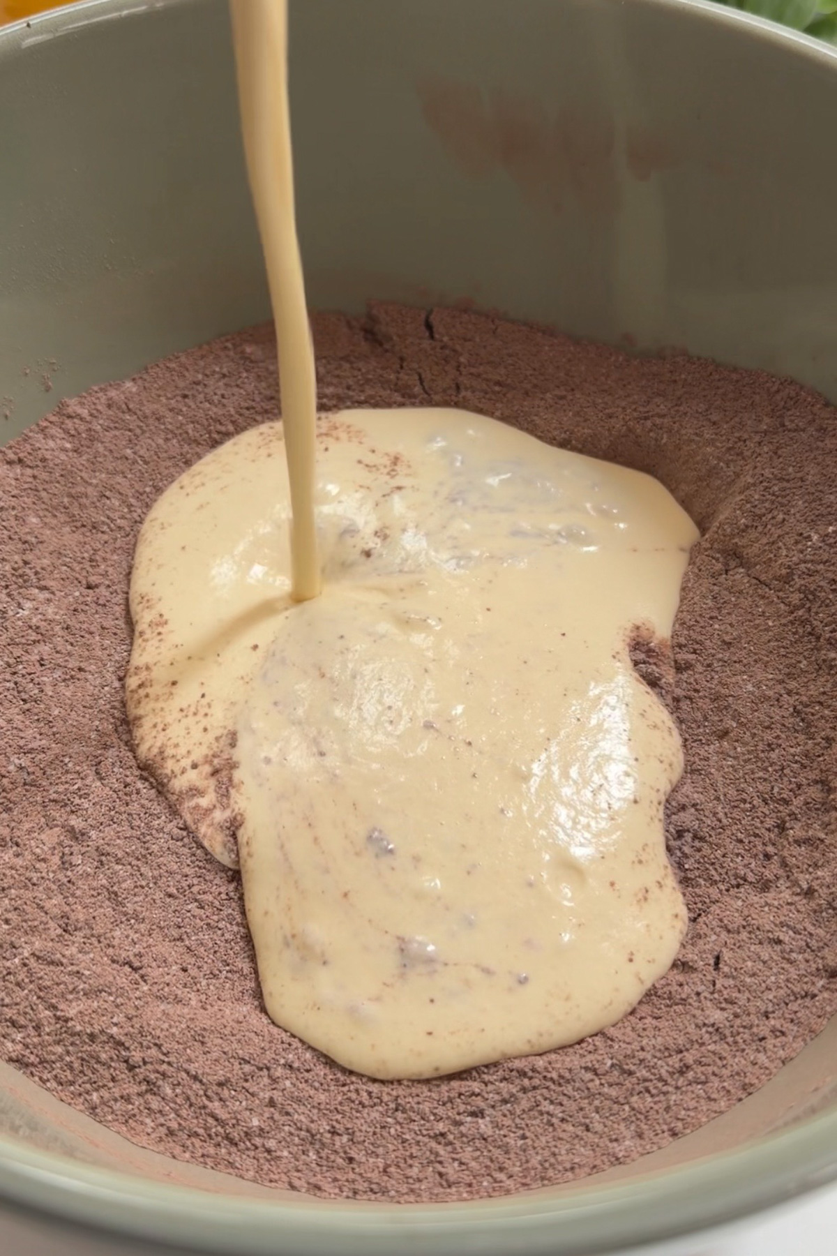Wet ingredients being added to the dry ingredients for a chocolate cream cheese sheet cake.