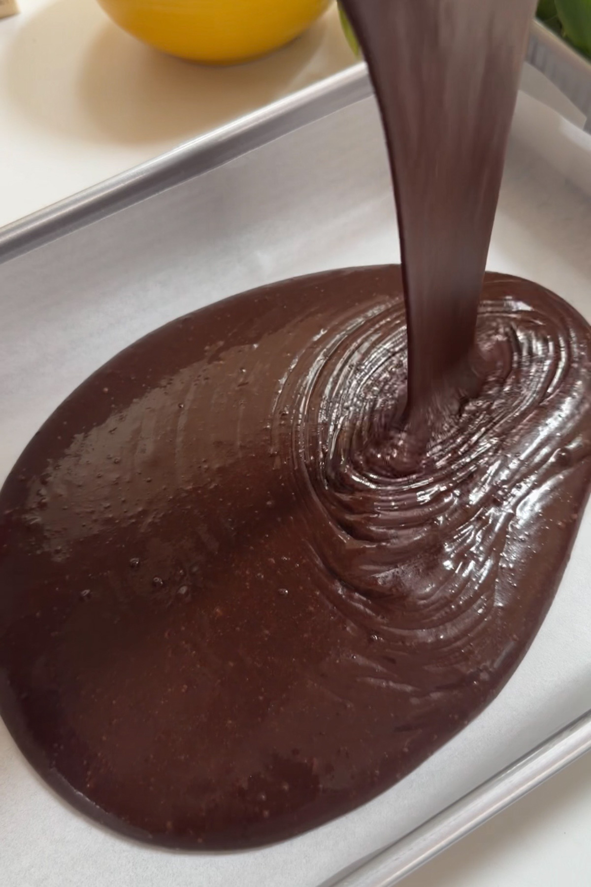 Chocolate cream cheese sheet cake batter being poured into a lined 9x13 baking pan.