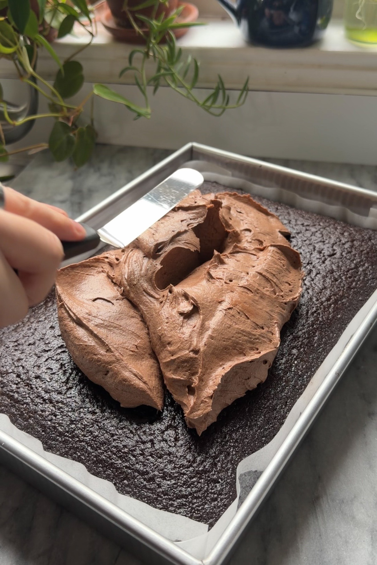 Chocolate cream cheese sheet cake in a 9x13 pan being decorated with chocolate cream cheese frosting.