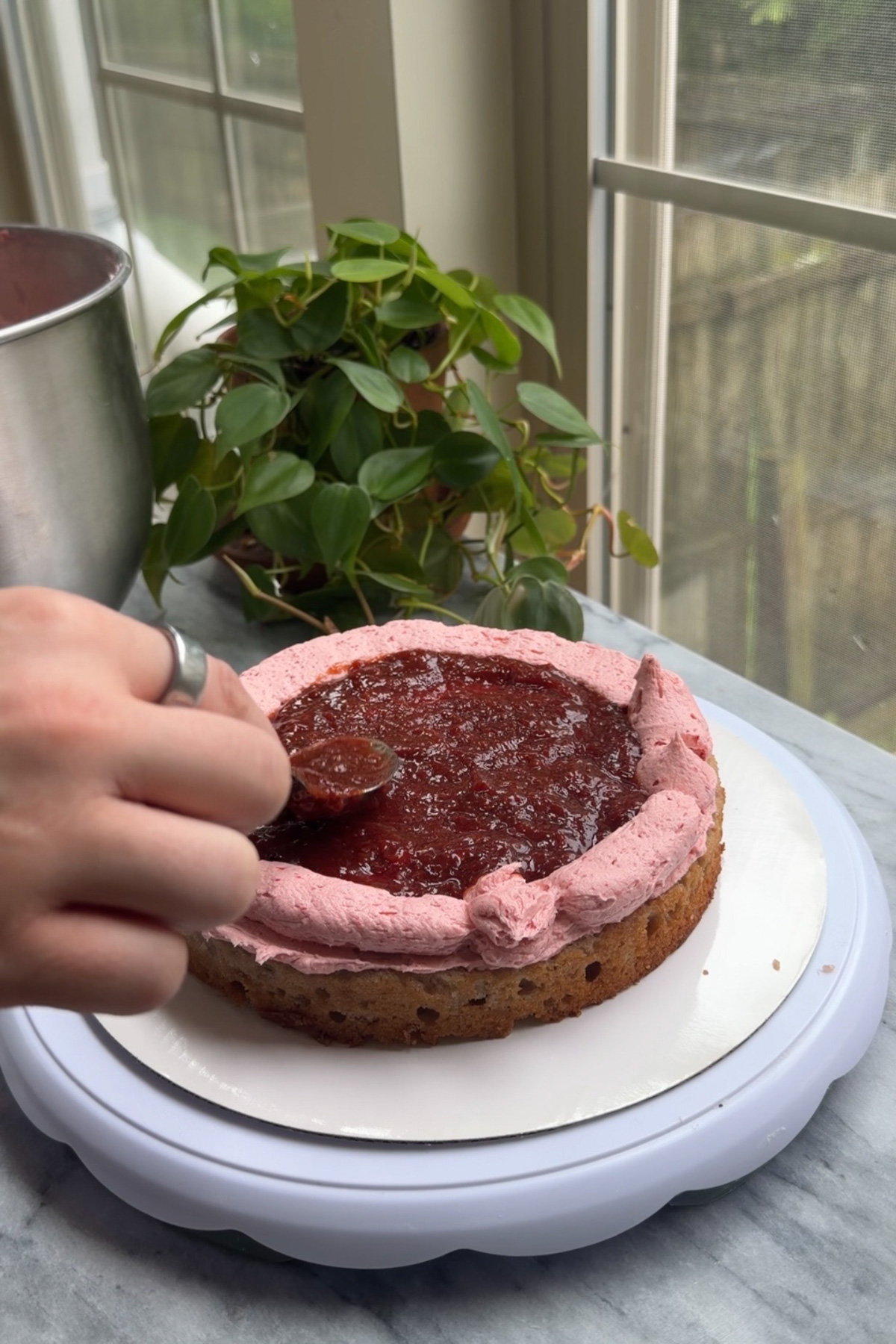The process of assembling a strawberry layer cake with strawberry filling by making a buttercream dam and filling the inside with strawberry compote.