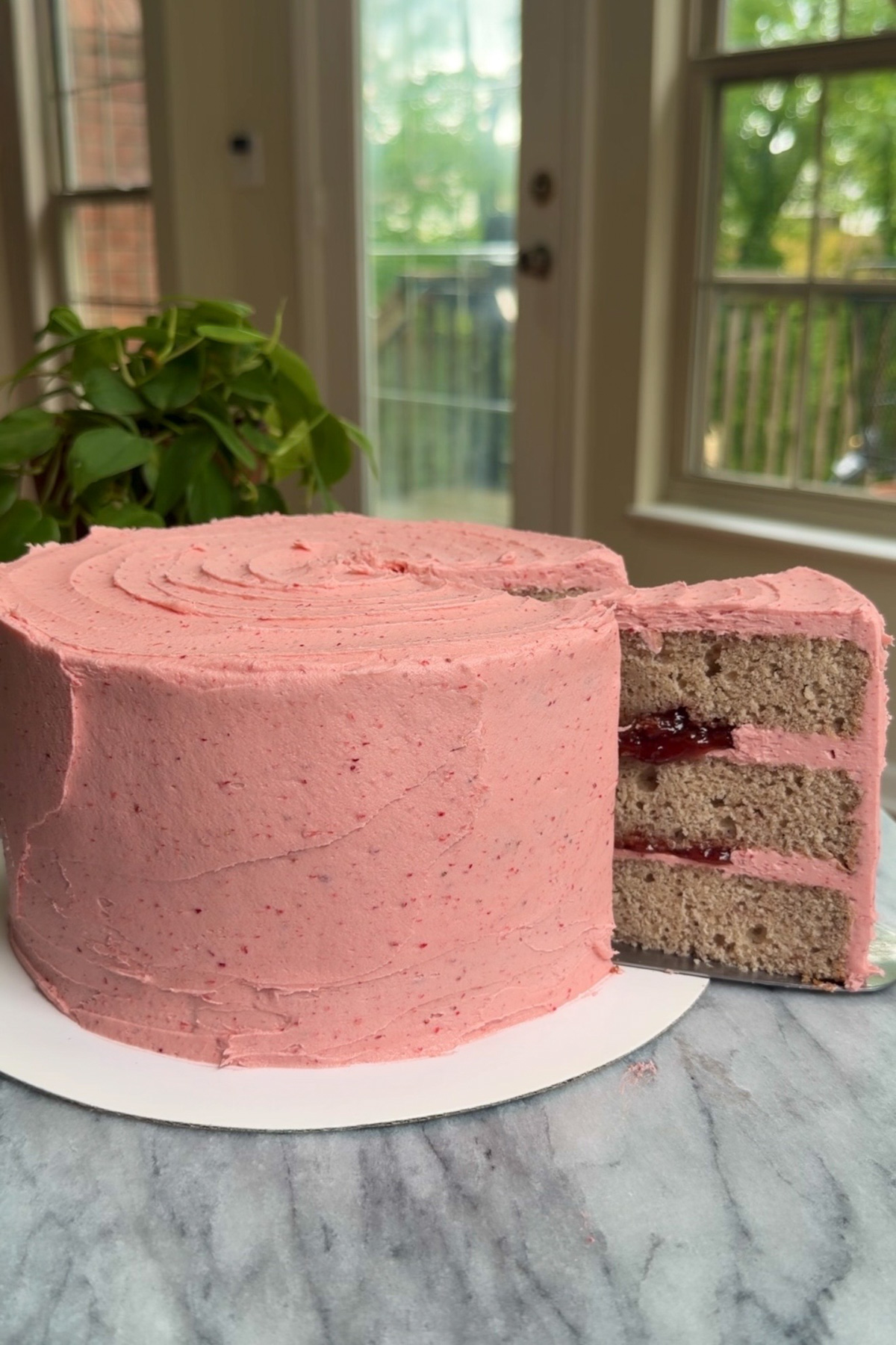 A strawberry layer cake with strawberry filling, with a slice being removed.
