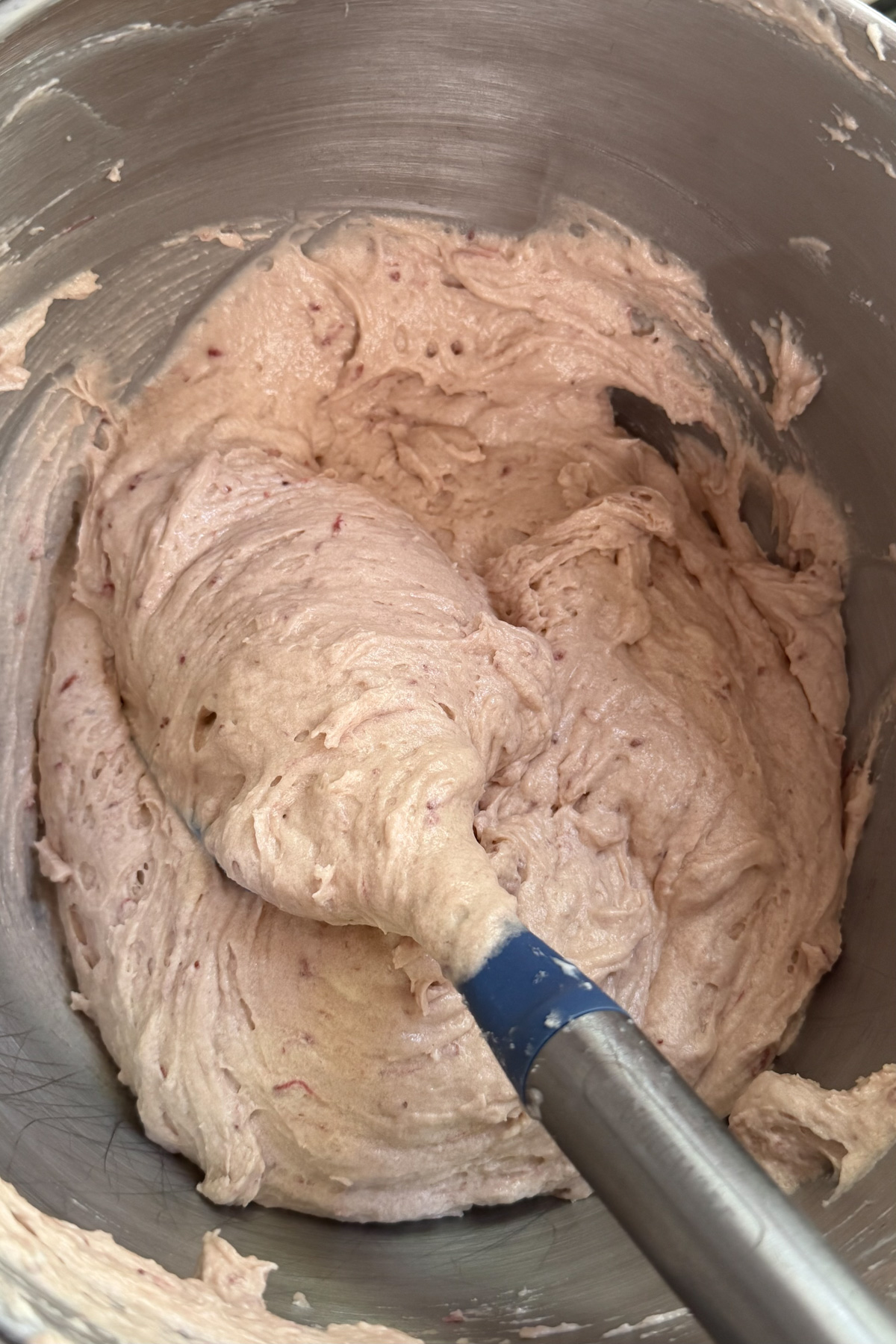 The batter for strawberry cake with strawberry filling in a stainless steel mixing bowl.