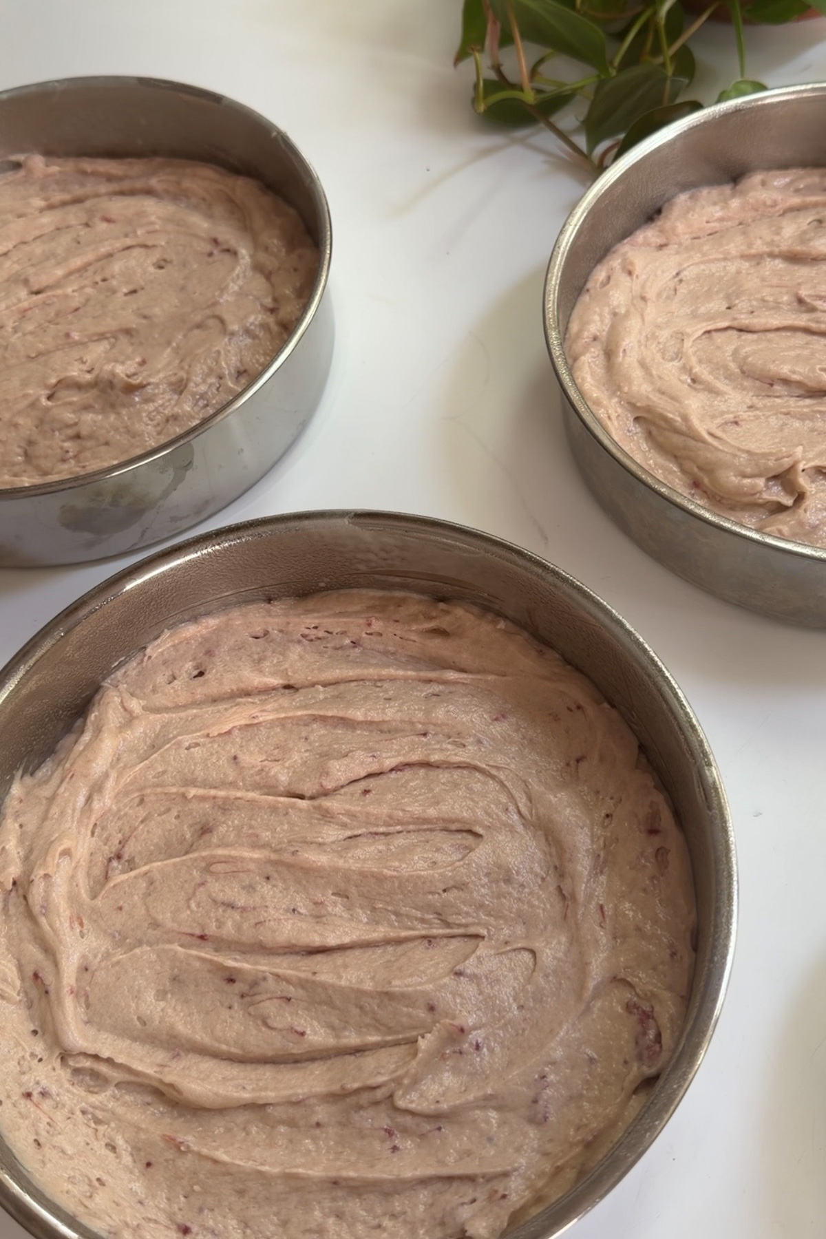 The batter for strawberry cake with strawberry filling divided between three prepared cake pans.