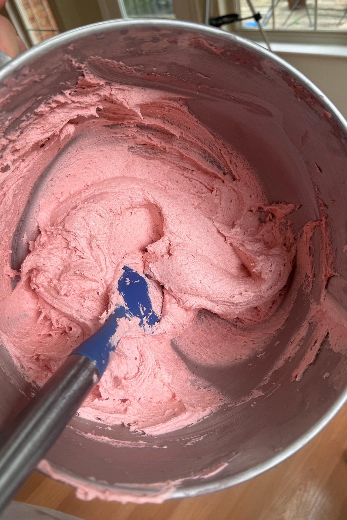 Strawberry buttercream for strawberry layer cake with strawberry filling in a stainless steel mixing bowl.