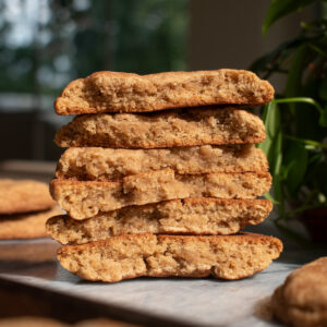 Three apple butter snickerdoodle cookies stacked on top of each other to show the chewy texture with a plant and window in the background.