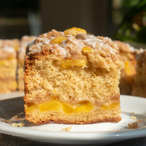 A slice of brown butter peach coffee cake on a white plate to show the layers of cinnamon streusel and peaches.