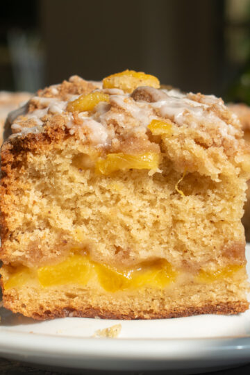 A slice of brown butter peach coffee cake on a white plate to show the layers of cinnamon streusel and peaches.