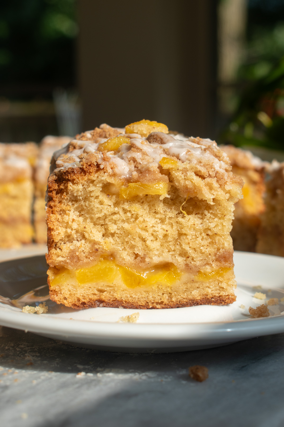 A slice of brown butter peach coffee cake on a white plate to show the layers of cinnamon streusel and peaches.